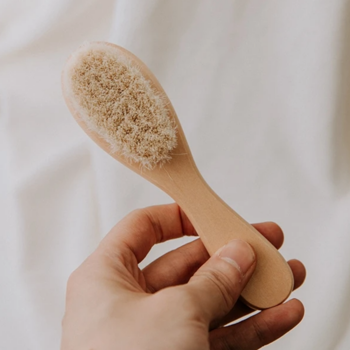 Eine Hand hält die Hello World Haarbürste - Weichborsten [4x15cm] für sanfte Pflege, mit weichen Borsten, vor einem neutralen, hellen Hintergrund.