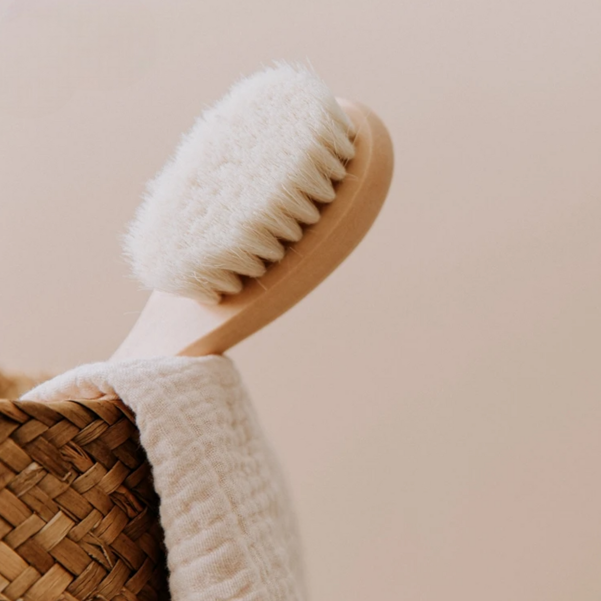 Eine Nahaufnahme der Hello World Haarbürste - Weichborsten [4x15cm] ruht auf einem geflochtenen Korb mit einem hellbeigen Handtuch vor einem neutralen Hintergrund, der an sanfte Pflege für Ihr Kind erinnert.