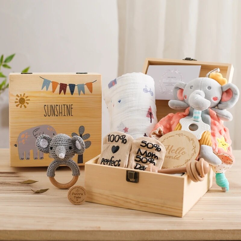 Das Cyrill Baby Geschenk zur Geburt von Hello World ist eine nachhaltige Holzbox mit der Aufschrift SUNSHINE, gefüllt mit Babyartikeln wie einem Plüschelefanten, einer Windel, einer gehäkelten Koala-Rassel, einem hölzernen Beißring und Socken, die charmant auf Holz angeordnet sind.