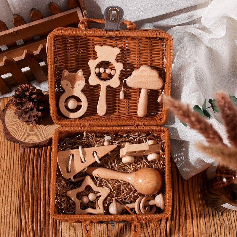 In einem geflochtenen Korb mit geöffnetem Deckel liegt das Dario Baby Geschenk zur Geburt von Hello World - Holzspielzeug in Form von Tieren, Bäumen, Sternen und Fahrzeugen - auf einer Strohfüllung auf einem rustikalen Holztisch neben Tannenzapfen und einem weißen Tuch arrangiert.