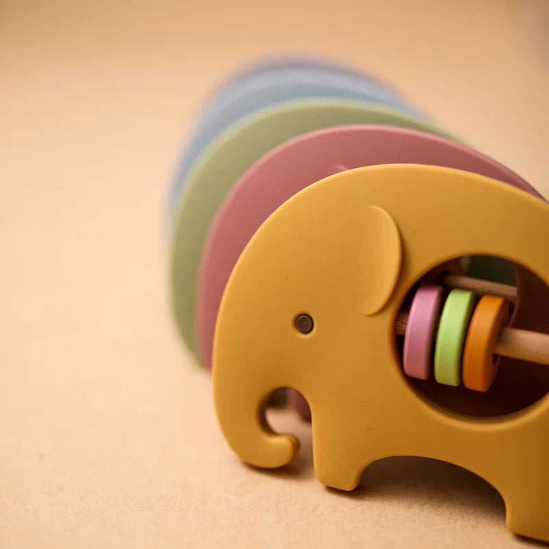 Eine Nahaufnahme des Hello World Elefant Gelb aus Silikon [9x6,8cm] Stapelspielzeugs mit kreisförmigen Ringen auf einem Holzstab, der auf einer beigen Oberfläche steht - ideal als niedliches Babyspielzeug für die Kleinsten.