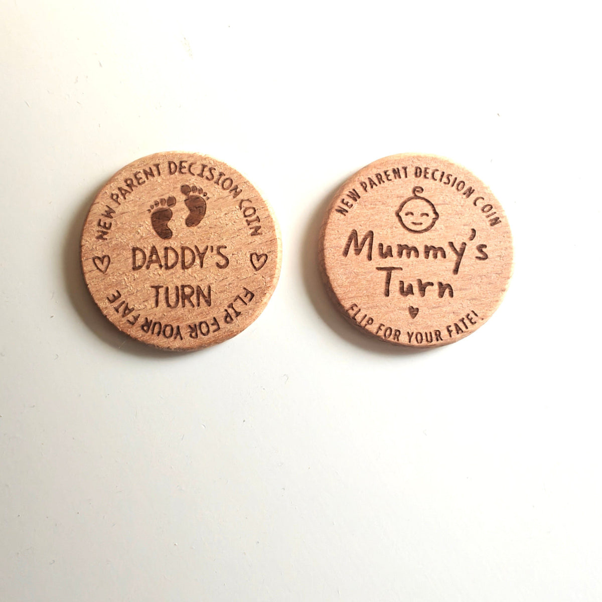 Zwei Hello World Entscheidungsmünzen (3,5 x 3,5 cm) ruhen auf einer weißen Fläche - auf einer steht "Daddy's Turn", auf der anderen "Mummy's Turn". Beide sind niedlich gestaltet und damit ein ideales Geschenk für frischgebackene Eltern, um Familienentscheidungen zu vereinfachen.