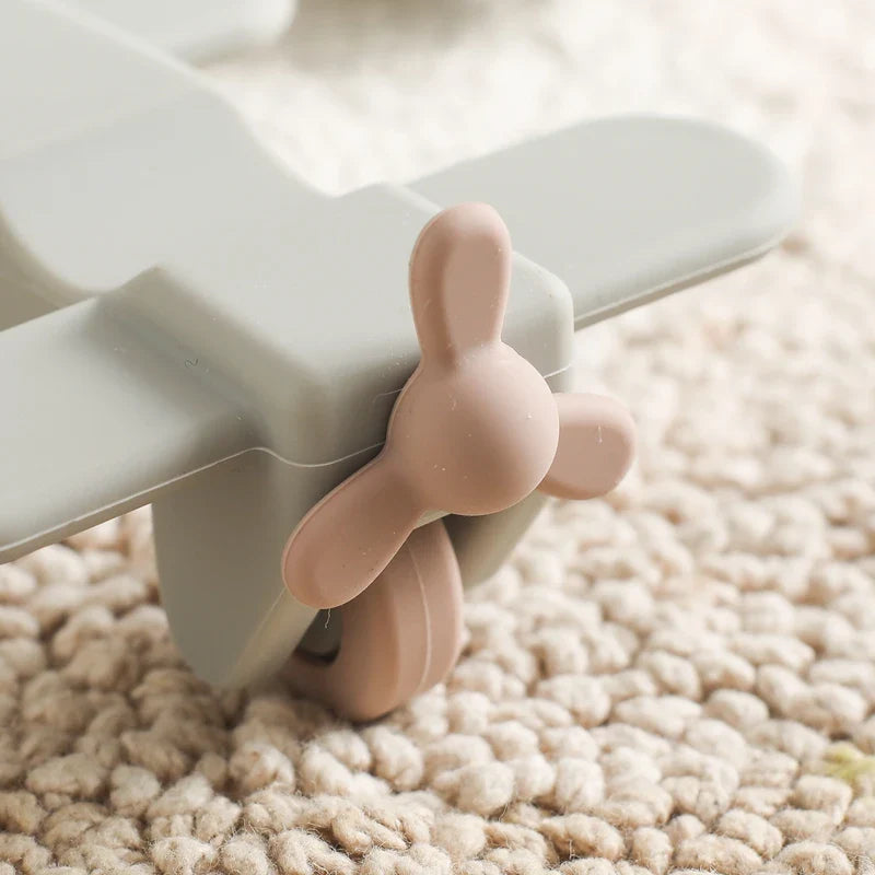 Eine Nahaufnahme des Hello World Flugzeugs aus Silikon [10,5x5,5cm], mit einem zart pastellfarbenen Propeller, ruht auf einem beigen Teppich. Dieses liebevoll gestaltete Babyspielzeug ist ideal für kleine Hände und sorgt für sicheres Spielen ab dem ersten Tag.