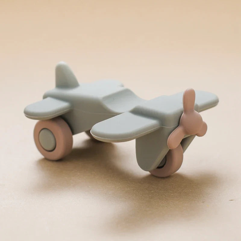 Ein minimalistisches Hello World Flugzeug aus Silikon [10,5x5,5cm] in Pastellgrau mit rosa Akzenten, aus glattem, mattem Silikon, auf beigem Hintergrund - das ideale Spielzeug für Kinder.