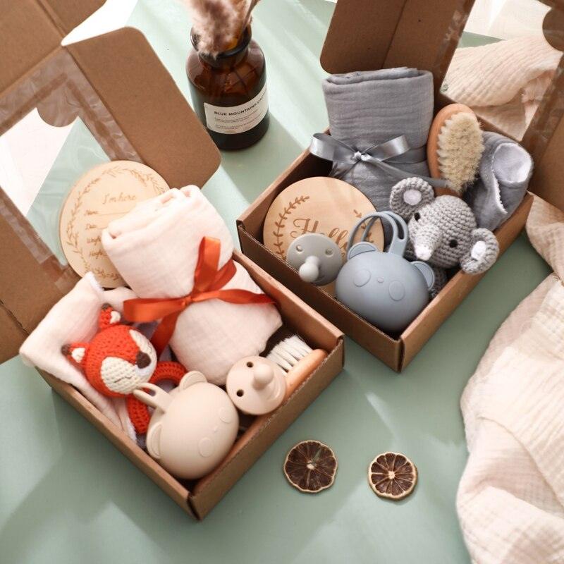 Zwei Hello World Gary Baby Geschenk zur Geburt Geschenkboxen mit Plüschtieren, einem Rasselelefanten, Schnuller-Set, Musselintüchern, Bürste, Holzscheibe und Schleife - hübsch arrangiert mit Trockenblumen und Zitrusscheiben.