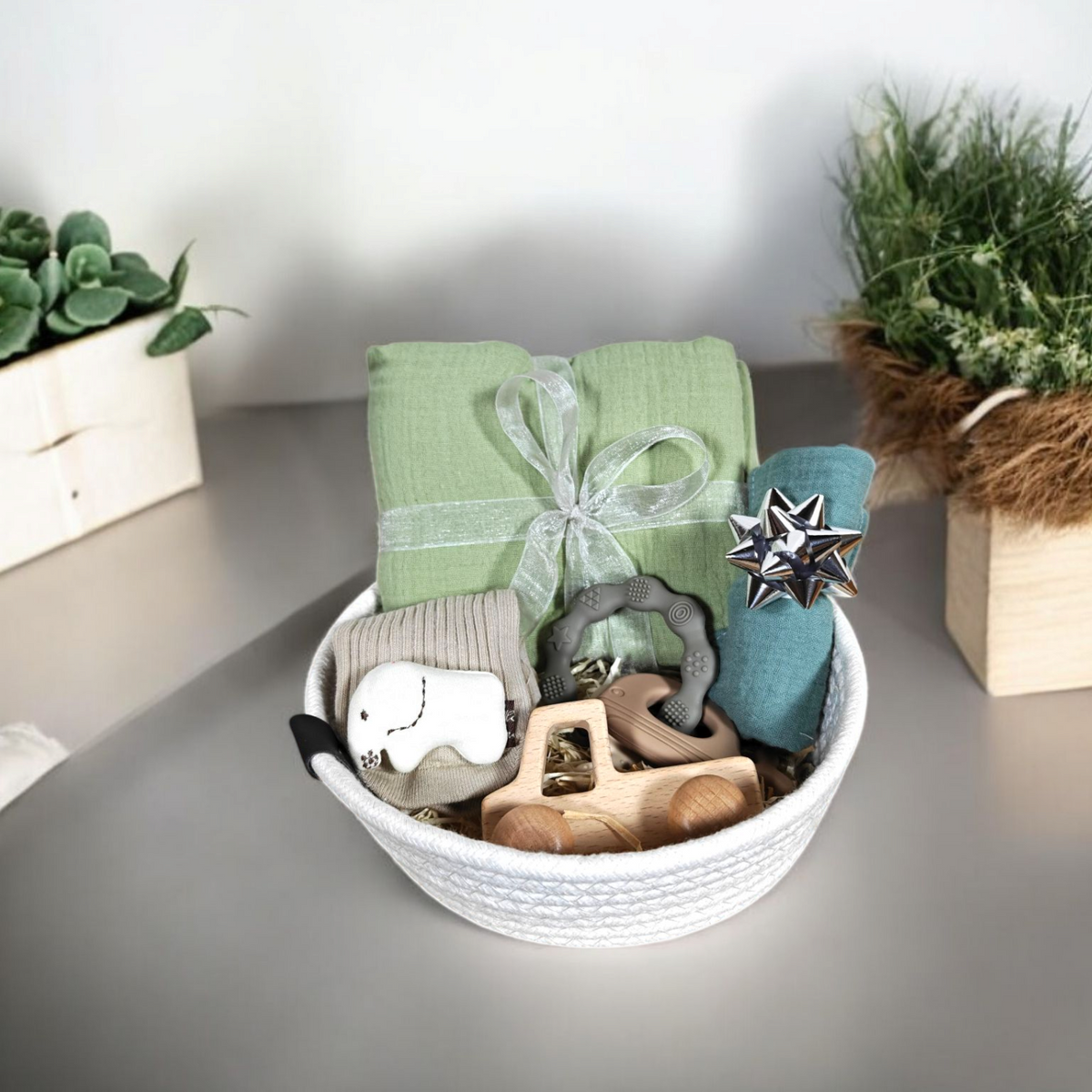 Das Geschenk Konfigurator Set von Hello World enthält grüne und blaue Tücher, Holzspielzeug, Beißring und einen kleinen Elefanten-Plüsch - liebevoll arrangiert. Entdecke personalisierte Baby-Geschenke mit Hello World!.