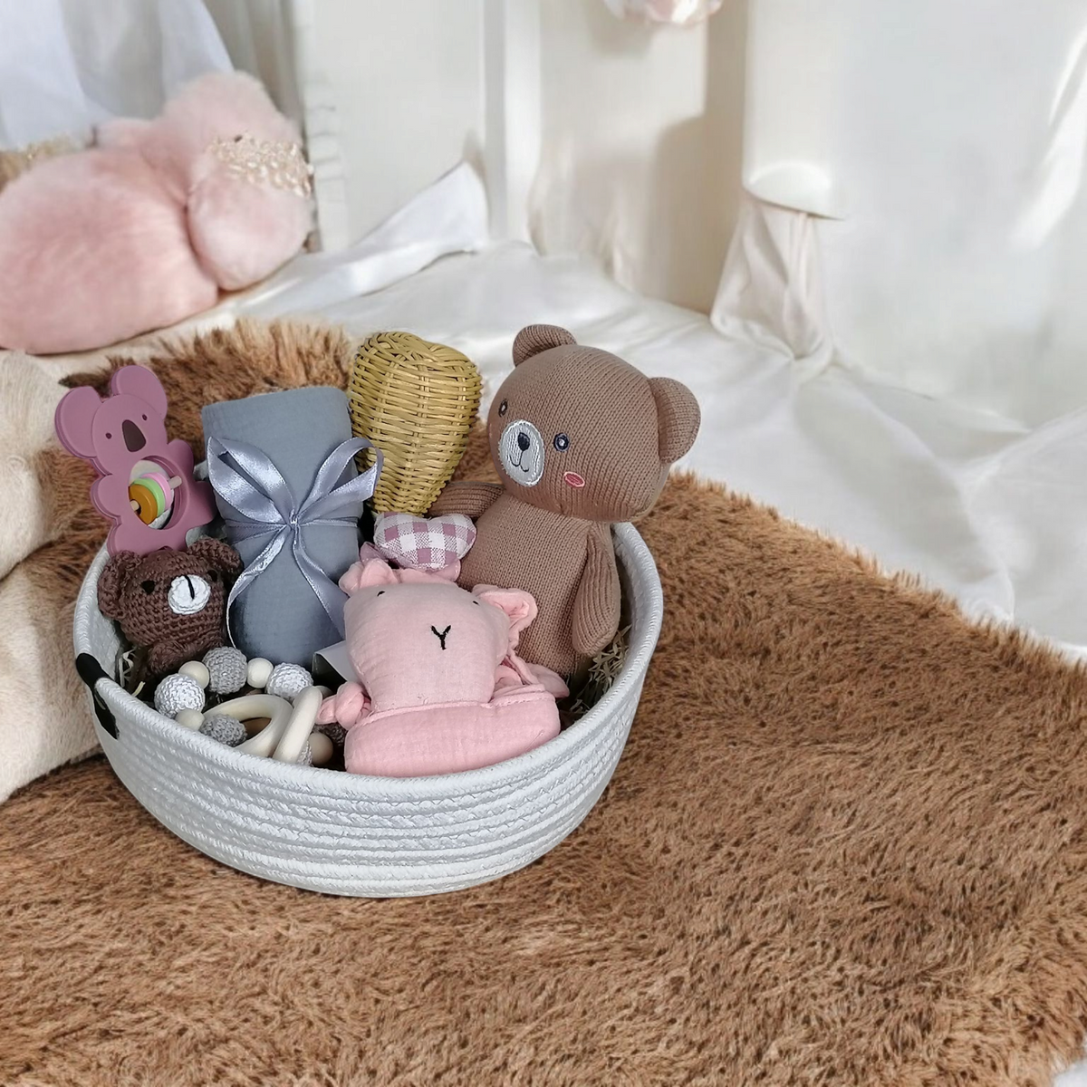 Ein weißer Korb mit Plüschtieren und Holzaccessoires aus dem Geschenk Konfigurator von Hello World steht auf einem braunen Teppich, umgeben von weichen Decken in einem gemütlichen, hellen Kinderzimmer.