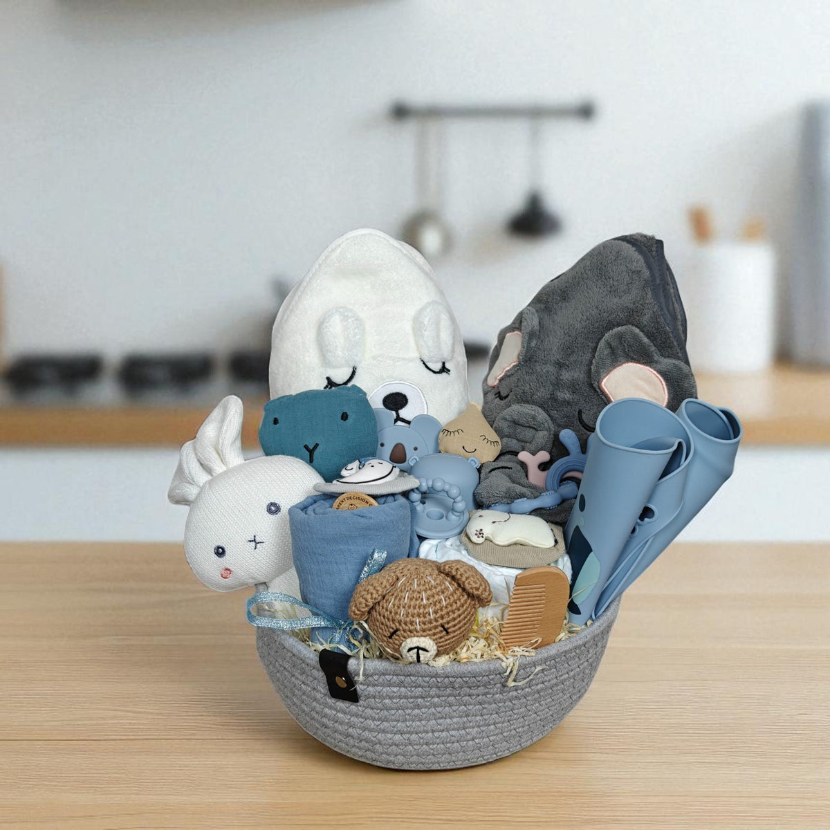 Ein geflochtener Korb mit Babyartikeln wie Plüschtieren und einem Handtuch steht auf einer Küchenzeile. Entdecke das Hello World Geschenk Konfigurator - gestalte individualisierte Geschenksets für Babys ganz einfach selbst!.