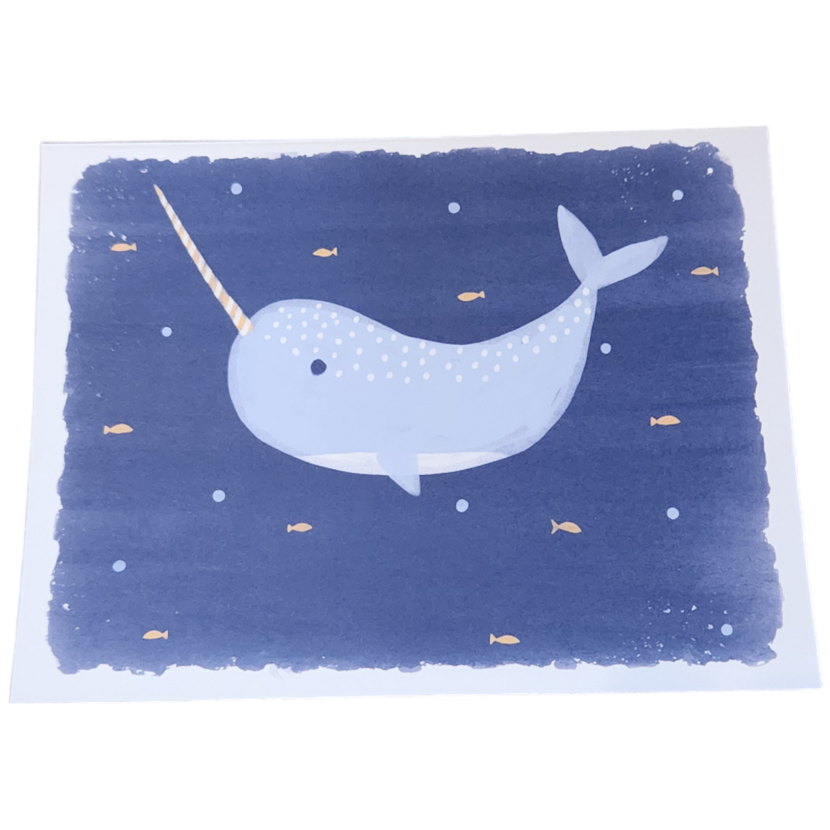 Die "Grusskarte Walfisch (Blau)" von Hello World zeigt einen niedlichen Cartoon-Einhornwal mit langem Stoßzahn, der zwischen gelben Fischen und Blasen in einem dunkelblauen Meer schwimmt, illustriert in einem verspielten, skurrilen Stil.