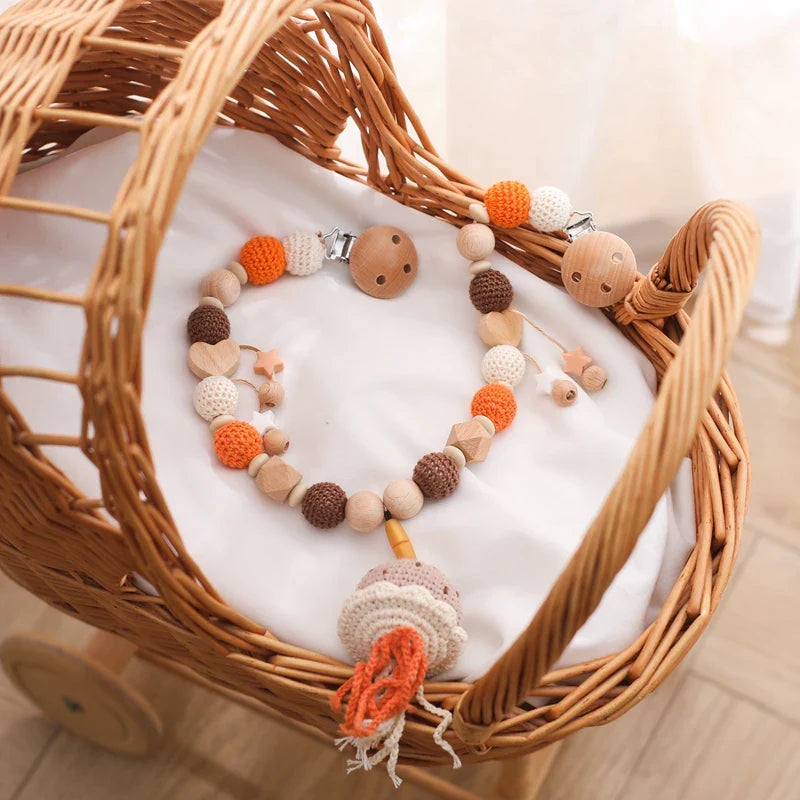 Die Hello World Kinderwagenkette Qualle [30x34cm] in beruhigendem Braun, Beige und Orange mit Tier- und Sternenmotiven ist in einem geflochtenen Stubenwagen mit weißem Kissen untergebracht - ideal für ein Kinderzimmer mit Unterwasserwelt-Thema.
