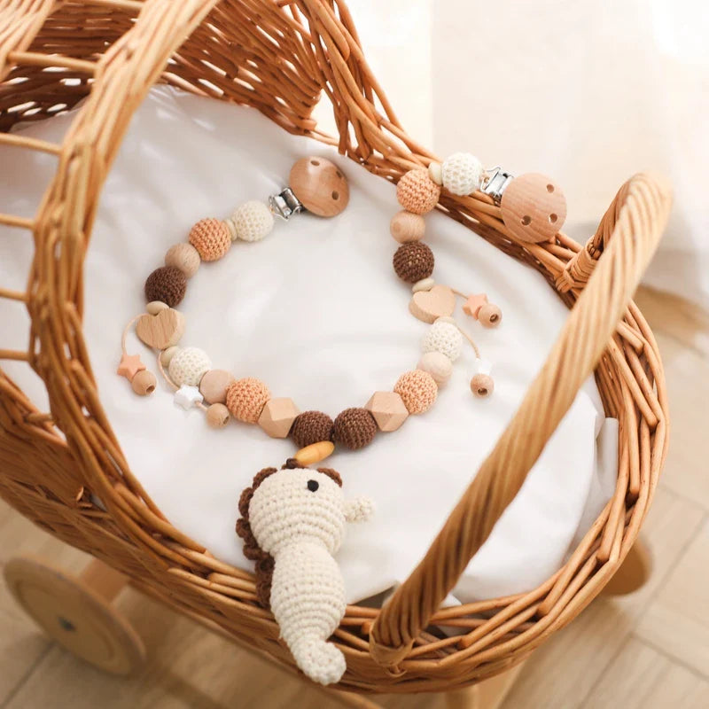 Ein geflochtener Rattan-Babykorb mit weicher weißer Matratze enthält ein gehäkeltes Löwenspielzeug und die Hello World Kinderwagenkette Seepferdchen [30x35cm], wodurch ein bezaubernder neutraler Look entsteht, der vom Unterwasserwelt Baby Thema inspiriert ist.