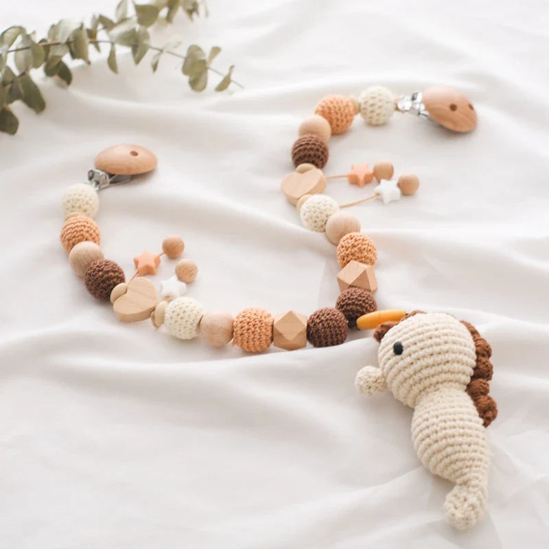 Die Hello World Kinderwagenkette Seepferdchen [30x35cm] besteht aus gehäkelten und hölzernen Perlen in neutralen Tönen mit einem plüschigen Seepferdchen, perfekt für Kinderzimmer mit Meeresmotiven. Das Seepferdchen ist auf weißem Stoff mit Eukalyptuszweigen abgebildet und bringt eine Unterwasserwelt-Baby-Atmosphäre mit sich.