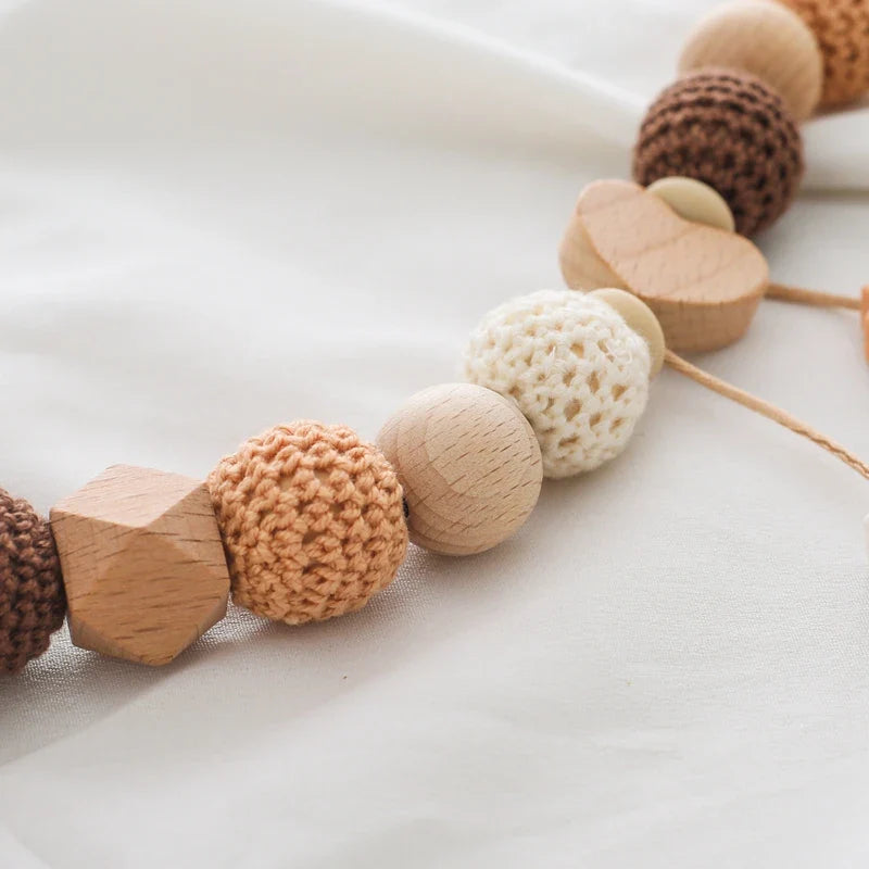 Eine Nahaufnahme der Hello World Kinderwagenkette Seepferdchen [30x35cm] zeigt hölzerne und gehäkelte Perlen in neutralen Tönen, die auf weichem weißem Stoff ruhen - ein ideales Kinderwagen-Accessoire für Ihr Kind.