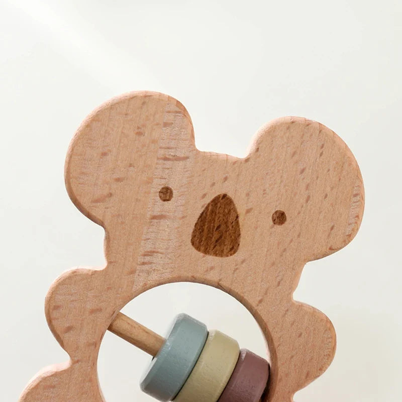 Der Koala aus Holz [7x15cm] von Hello World ist eine nachhaltige Baby-Rassel mit schlichtem Gesicht und drei pastellfarbenen Ringen - ideal fürs australisch inspirierte Kinderzimmer, dekorativ vor hellem, minimalistischem Hintergrund.