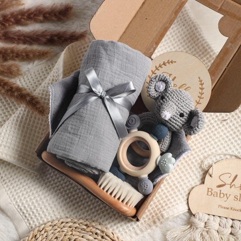 Das "Liam Baby Geschenk zur Geburt" von Hello World besteht aus einem gefalteten grauen Multifunktionstuch, einer Babybürste aus Holz, einem gehäkelten Koala, einem Holz-Silikon-Beißring und einer runden Holztafel auf beigem Stoff.