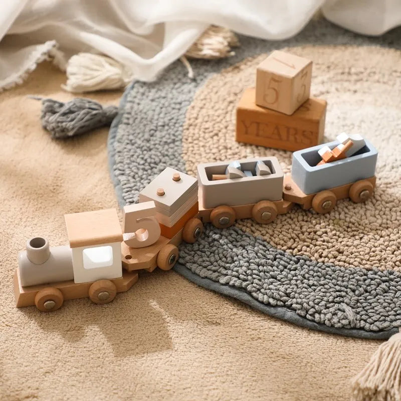 Eine Hello World Lokomotive aus Holz [34,5x6,4cm] mit drei Autos sitzt auf einem strukturierten runden Teppich, umgeben von Blöcken - darunter einer mit der Aufschrift "5 YEARS" - und kleinen Holzformen aus nachhaltigem Naturholz in gemütlichen neutralen Farben und sanftem Licht.
