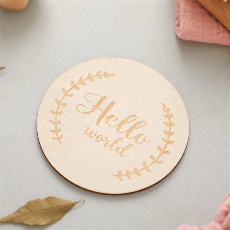 Das Lora Baby Geschenk zur Geburt von Hello World ist eine runde Holztafel mit der Gravur "Hello world" und blättrigen Zweigen, ideal zum Verschenken neben Beißringen oder einem Holz-Greifling.
