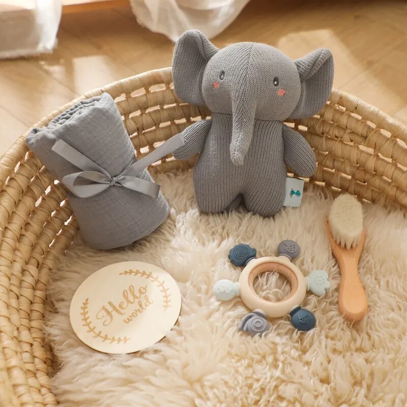 Das Matteo Baby Geschenk zur Geburt von Hello World besteht aus einem Weidenkorb mit einer grauen, zusammengerollten Decke, einem Plüschelefanten, einem blau-grauen Holz-Silikon-Beißring, einer Baby-Haarbürste und einer Holzplakette mit dem Schriftzug "Hello world" - ideal als Geschenk für Neugeborene.