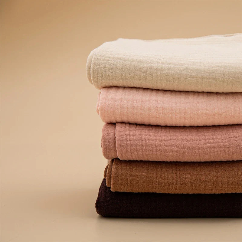 Ein ordentlich gestapelter Stapel von vier Hello World Multifunktionstüchern Beige [55x65cm] - perfekt als Spucktuch oder Stilltuch - in Creme-, Rosé-, Mauve- und Dunkelbrauntönen auf einem einfarbig beigen Hintergrund.