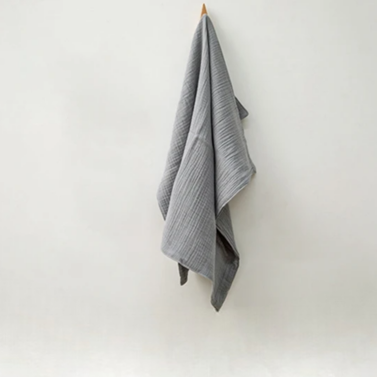 Das Multifunktionstuch Grau [55x65cm] von Hello World hängt ordentlich an einem Haken vor weißer Wand und sorgt für einen minimalistischen Look - ideal auch als Stilltuch.