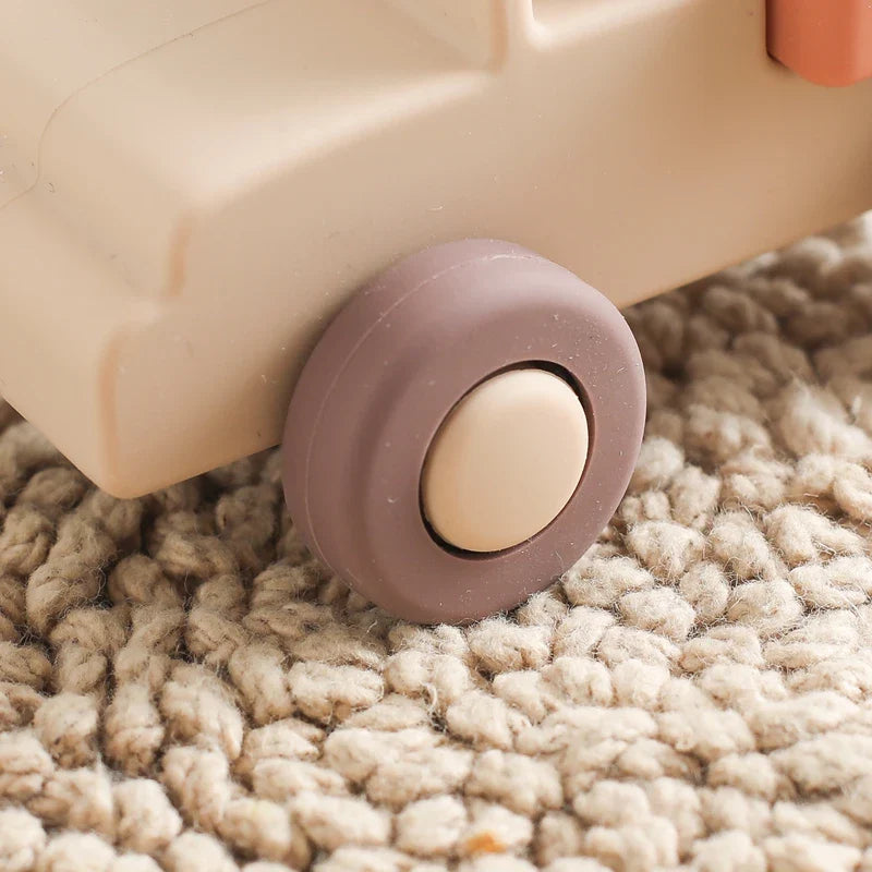 Nahaufnahme des Spielzeugautorads Pickup Beige aus Silikon [11x5cm] von Hello World auf einem strukturierten beigen Teppich. Das hellbraune Silikonauto hat einen braunen Reifen und eine beige Radkappe, perfekt für fantasievolles Spiel.