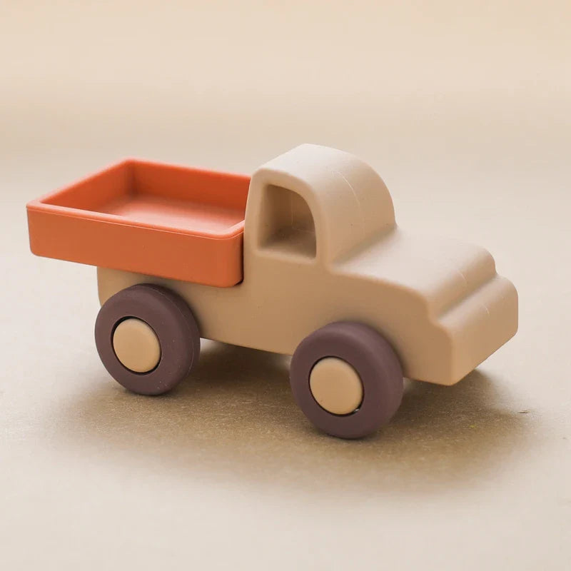 Der Hello World Pickup Beige aus Silikon [11x5cm] zeigt ein beiges Fahrerhaus, lila Räder und eine orangefarbene Ladefläche auf einer neutralen beigen Oberfläche.