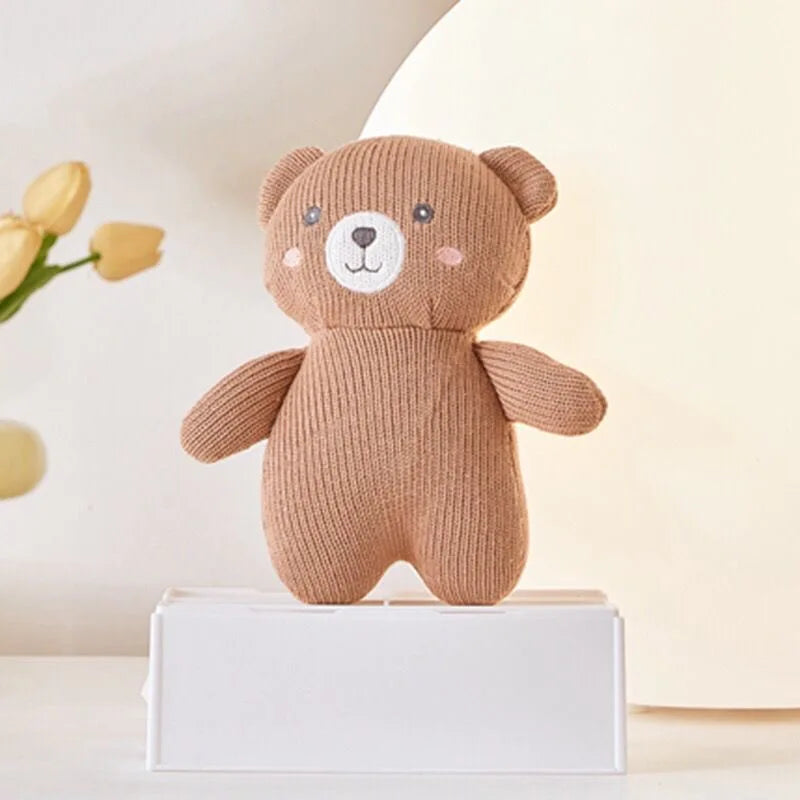 Das Plüschtier Bär [17x16cm] von Hello World ist ein weicher, brauner Teddy mit weißer Schnauze und rosa Bäckchen. Es steht auf einer weißen Box, umgeben von gelben Blumen und sanft verschwommenem Hintergrund - perfekt für Kinder.