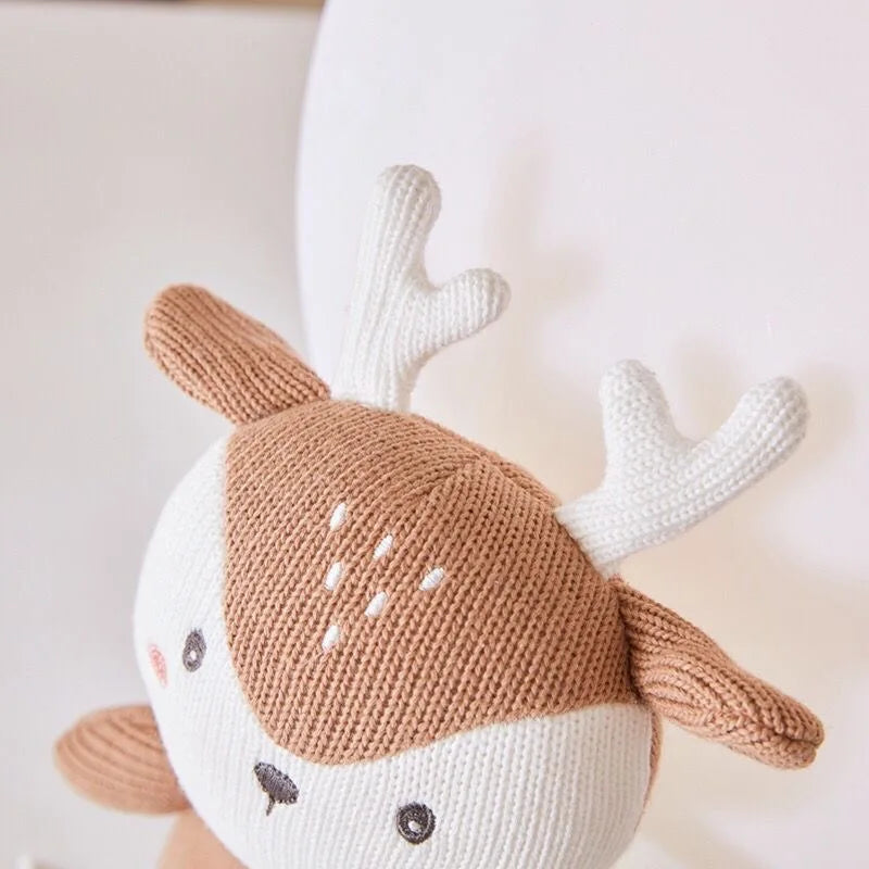 Eine Nahaufnahme des Hello World Plüschtier Hirsch [16x20cm], handgestrickt aus braunem und weißem Garn, mit weißem Geweih und einfachen gestickten Merkmalen, vor einem neutralen Hintergrund.