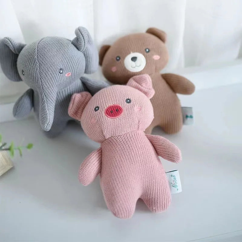 Drei weiche, gestrickte Stofftiere - darunter das Hello World Plüschtier Schweinchen [18x14cm], ein brauner Bär und ein grauer Elefant - liegen auf einer weißen Fläche in einem hell erleuchteten Raum.