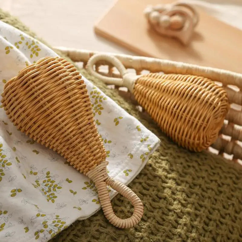 Zwei Rassel Rattan [8x17cm] von Hello World mit Loop-Griffen liegen auf einer grünen Decke und einem weißen Tuch mit Blumenmuster - nachhaltige Musikinstrumente vor einem Holzspielzeug auf hellem Hintergrund.