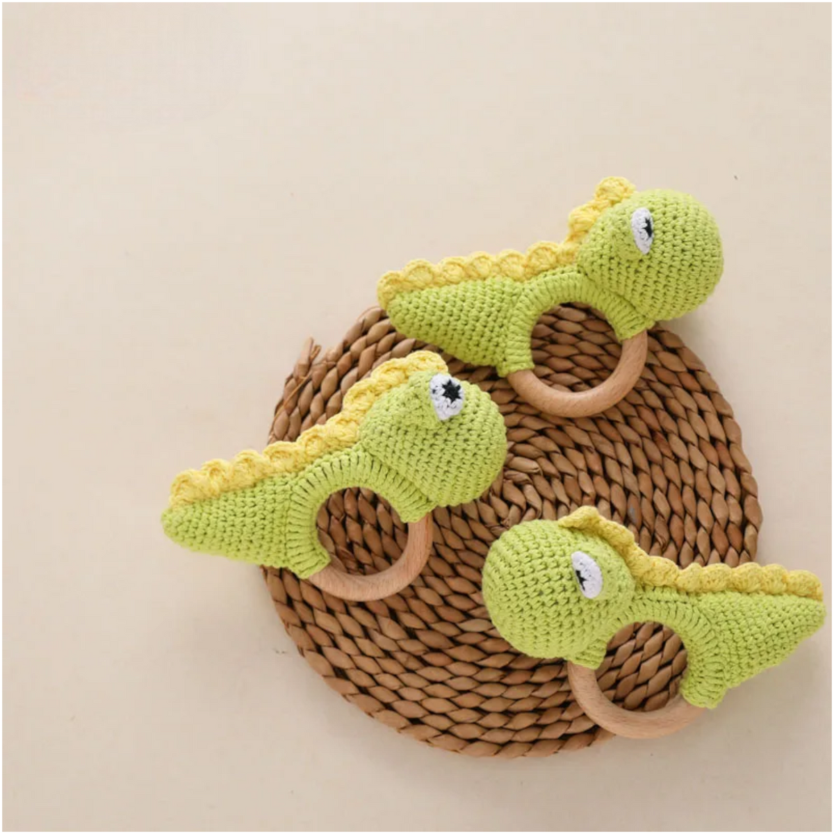 Drei grüne Rasseltier Dino [10x14cm] von Hello World mit Holzringen liegen auf einer runden Matte vor hellem beigem Hintergrund - ein bezauberndes Dinosaurier-Spielzeug und Rassel für Kinder.