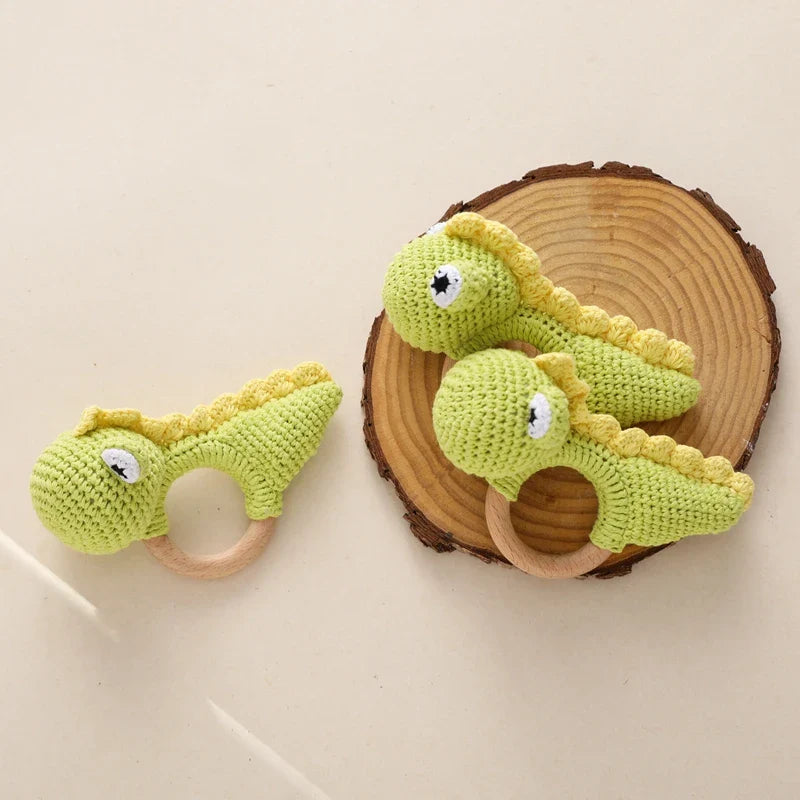 Drei grüne Hello World Rasseltier Dino [10x14cm] Rasseln mit gelben Stacheln und Holzringen sind auf einer hellen Fläche ausgestellt - zwei auf einer Holzscheibe, eine in der Nähe - ideal als einzigartiges Dino-Babyspielzeug.