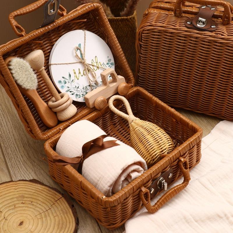 Das Rusty Baby Geschenk zur Geburt von Hello World besteht aus einem offenen Weidenkoffer mit einem gerollten Handtuch, einem Holzauto, einer Bürste, einer Rassel und einem runden Blumenteller für Meilenstein-Karten; daneben befindet sich ein weiterer geschlossener Koffer - perfekt zum Verschenken.