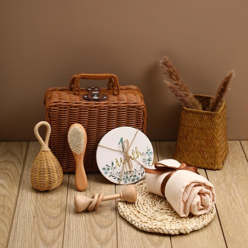 Das Rusty Baby Geschenk zur Geburt von Hello World besteht aus einem Picknickkorb, einer Bürste, einer Rassel, Meilensteinkarten, einer zusammengerollten Decke, einem Holzspielzeug, einer geflochtenen Matte und einer Vase mit getrockneten Gräsern - wunderschön arrangiert als perfektes Geschenk für Neugeborene.