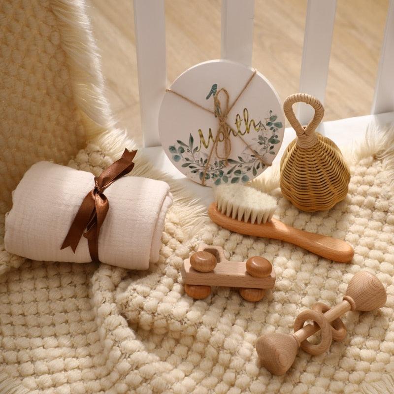 Das Rusty Baby Geschenk zur Geburt von Hello World besteht aus einer weichen beigen Decke, einem Holzauto und einer Rassel, einem Musselintuch, das mit einem braunen Band gebunden wird, und charmanten Details - perfekt zum Verschenken auf einem strukturierten Teppich.