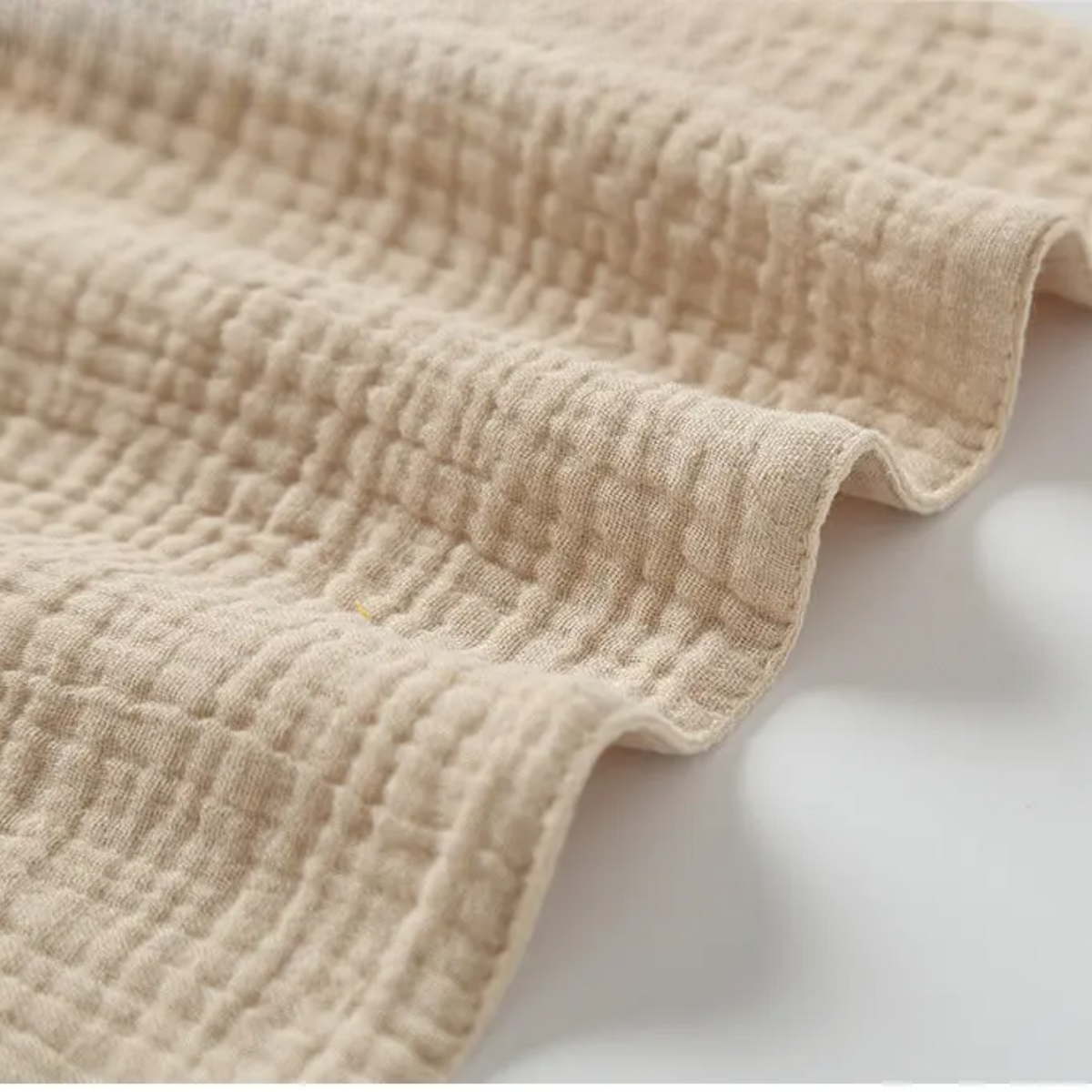 Eine Nahaufnahme des Schnuffel Beige [33x46cm] von Hello World zeigt seine weiche, gesteppte Textur und den gewellten Rand. Der leichte beigefarbene Stoff hat ein sanftes Gittermuster und liegt glatt auf einer weißen Oberfläche.