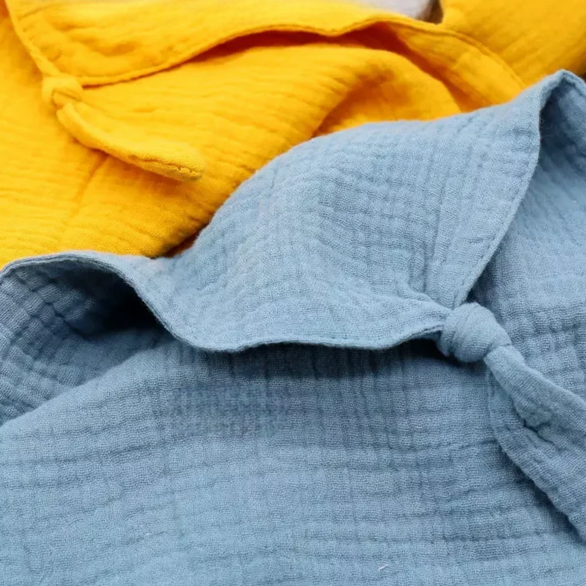 Nahaufnahme des strukturierten Stoffes aus der Hello World Schnuffel Orange [33x46cm], mit weichen gelben und hellblauen Tüchern in einfachen Knoten - ideal als kuscheliges Kuscheltier oder gemütliches Kindergeschenk.