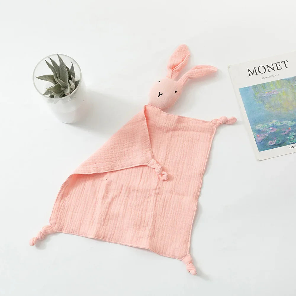 Eine rosa Schnuffel Rosa [33x46cm] Baby-Kuscheldecke von Hello World liegt auf einer weißen Fläche neben einer getopften Sukkulente und einer Zeitschrift mit Monets Kunst - ein bezauberndes Baby-Geschenk.