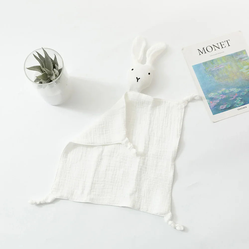Ein Schnuffel Weiss [33x46cm] Musselintuch von Hello World mit einem Hasenkopf ruht auf einer weißen Fläche neben einer kleinen Sukkulente und einem Monet-Kunstbuch - ein entzückendes Babygeschenk.