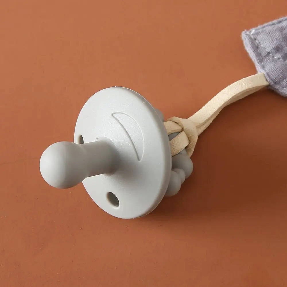 Ein blauer Hello World Schnuller Blau [4,5x6cm] mit rundem Schild und geknotetem Band ruht auf einer braunen Oberfläche - eine niedliche Geschenk Babyparty Idee.