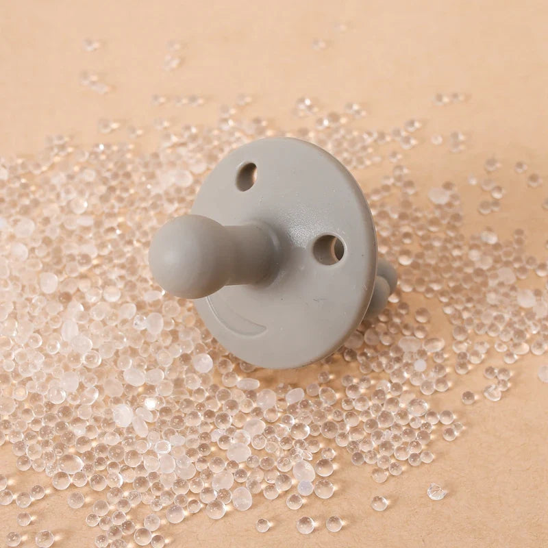 Ein Schnuller Grau [4.5x6cm] der Marke Hello World liegt stilvoll auf einer Perlen-bedeckten Oberfläche - ein Bild moderner Eleganz.