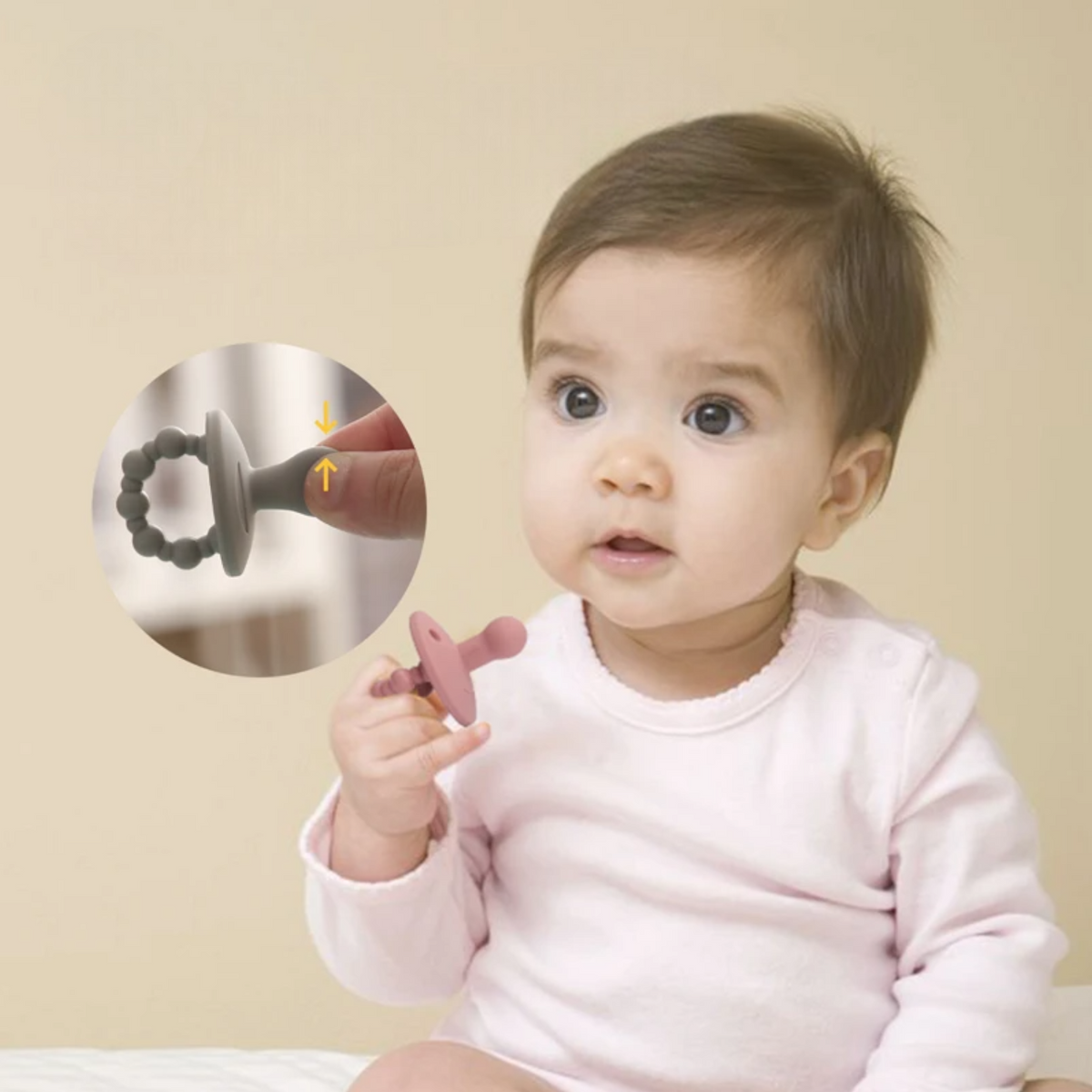 Ein Baby in einem hellrosa Outfit hält den Hello World Schnuller Pink [4,5x6cm] Schnuller. Ein Einsatz zeigt den biegsamen Rundgriff, der ihn zur perfekten Beruhigungshilfe macht, vor einer schlichten beigen Wand.