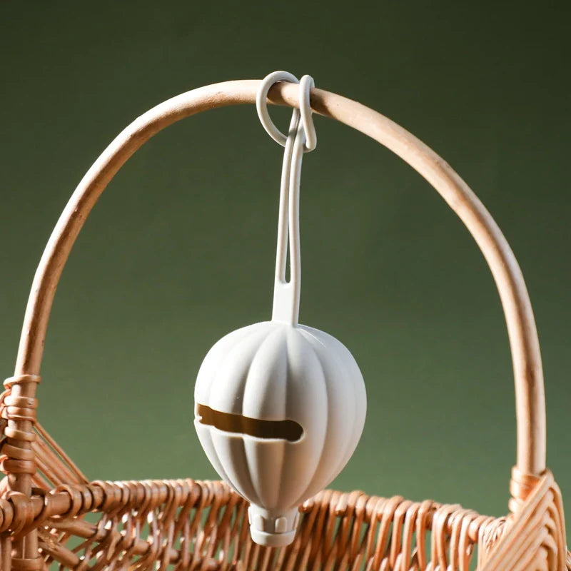 Die Hello World Schnullertasche Heissluftballon Blau [7x22,5cm] hängt an einem geflochtenen Korbgriff, perfekt für die Schnuller-Aufbewahrung - ein charmantes Baby-Geschenk vor grünem Hintergrund.