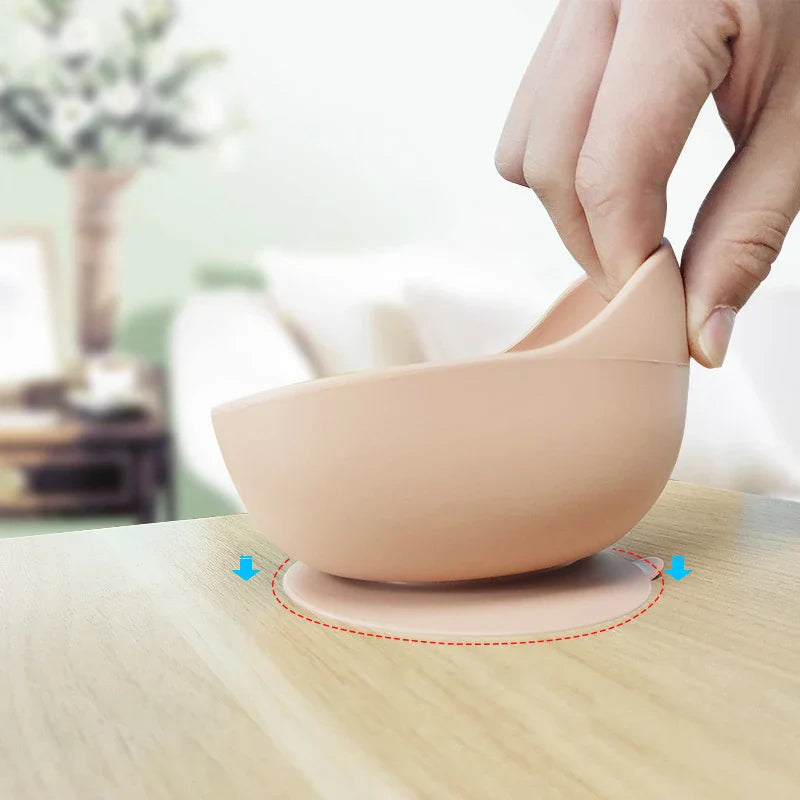 Eine Hand hebt eine Hello World Schüssel rund Beige [12x8cm] mit starkem Saugfuß aus Holz. Blaue Pfeile und ein rot gepunkteter Kreis heben die Schüssel hervor. Im Hintergrund ist ein verschwommenes Wohnzimmer mit Blumen zu sehen.