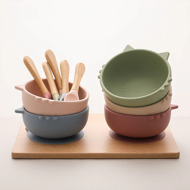 Die Hello World Schüssel rund Katze Grün [12x5cm] steht auf einem Holzbrett, gepaart mit Löffeln mit Holzgriff. Das niedliche Katzenohren-Design und die Pastellfarbe verleihen der Szene einen süßen, minimalen Touch.