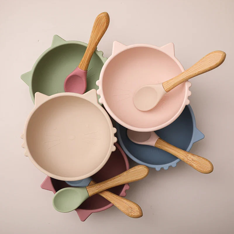 Fünf Hello World Schüsseln "Schüssel rund Katze Rosa" [12x5cm] mit je einem Silikonlöffel mit Holzgriff sind überlappend auf einem hellen Hintergrund angeordnet - der ideale Silikon-Babyteller für Baby-Led Weaning.