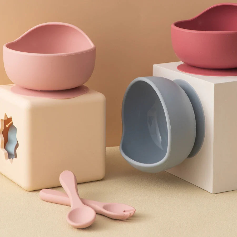 Die Schüssel rund Rosa [12x8cm] von Hello World erstrahlt auf minimalistischen beige-weißen Blöcken, während zwei passende pinke Löffel im Vordergrund liegen - ein echtes Highlight für stilvolle Mahlzeiten.