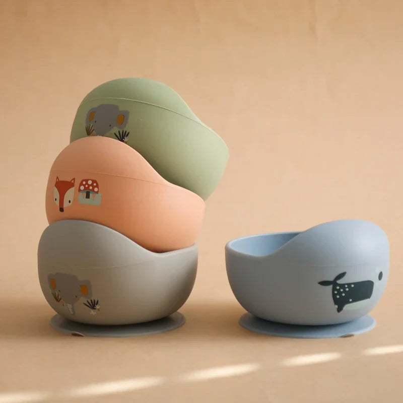 Vier pastellfarbene "Hello World" Schüsseln sind links gestapelt, rechts steht einzeln die "Schüssel rund mit Motiv Blau [12x8cm]" mit Walfisch-Motiv vor neutralem Hintergrund.