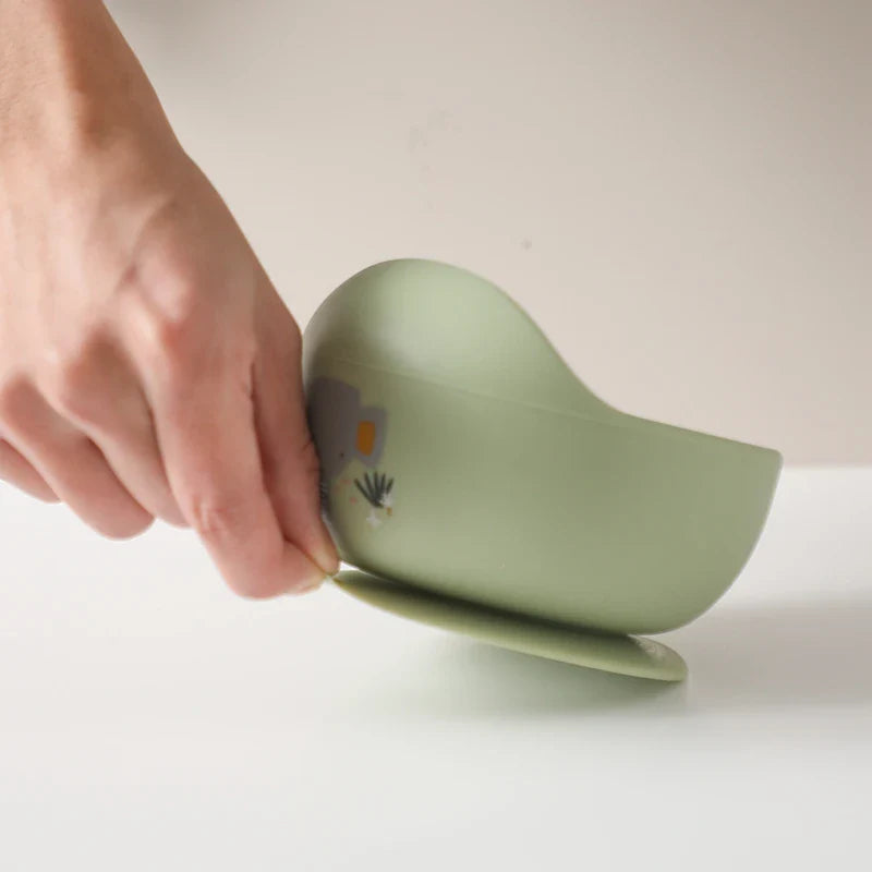 Eine Hand hebt den Rand einer Hello World Schüssel rund mit Motiv Grün [12x8cm] mit Saugfuß an und demonstriert damit ihren sicheren Halt auf einer weißen Oberfläche.