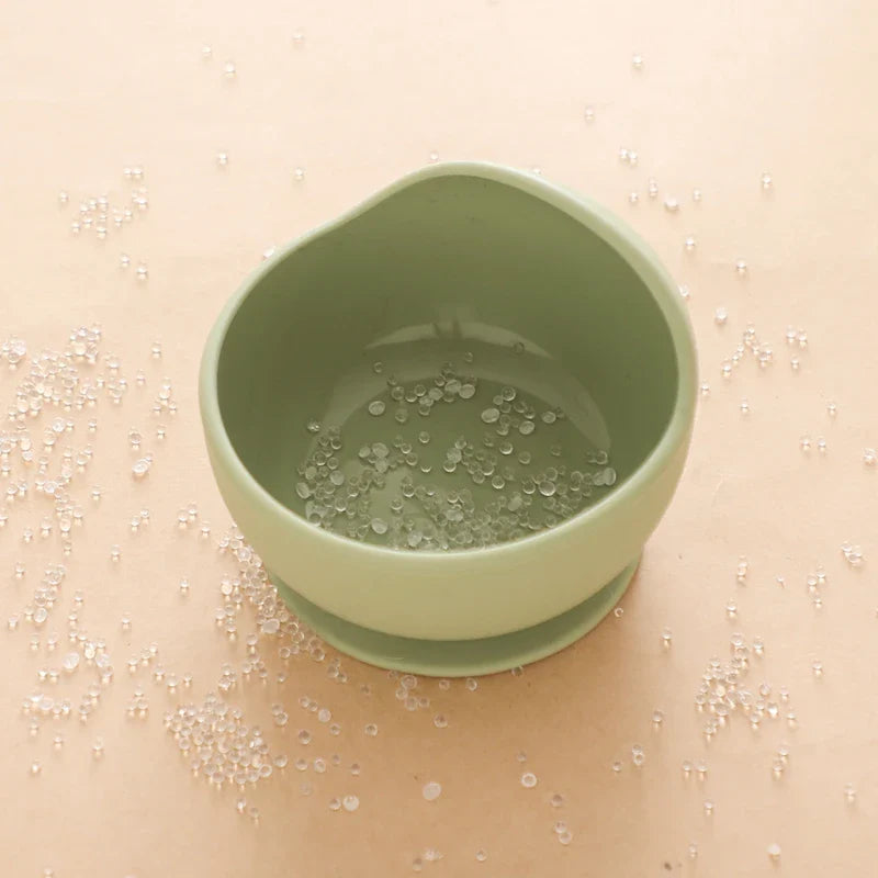 Eine Hello World Schüssel rund mit Motiv Grün [12x8cm] steht auf einer hellbeigen Fläche, gefüllt mit kleinen klaren Perlen, die auch ringsum verstreut liegen.